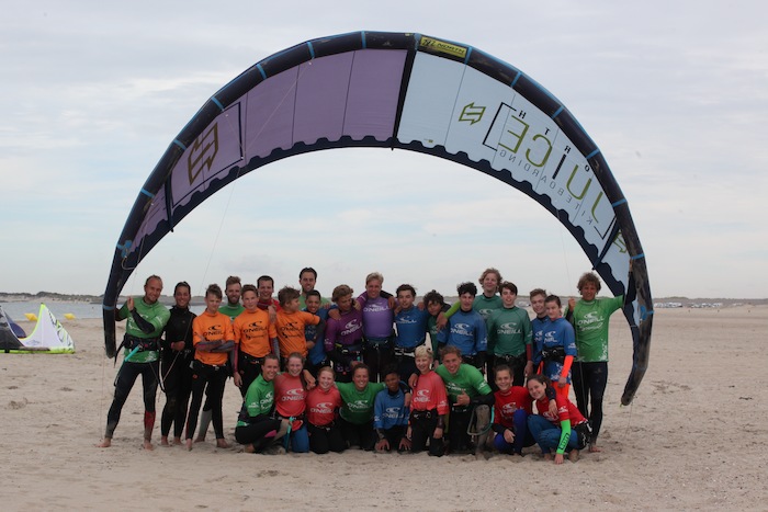 Jongeren poseren op het strand met een kite tijdens het kitesurfkamp in Zeeland.