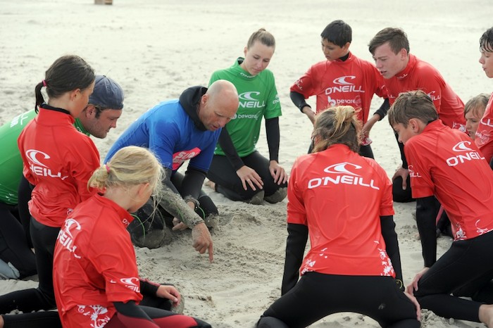 Begeleider geeft uitleg aan groepje kinderen op surfkamp