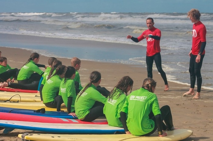 Kinderen krijgen uitleg van een surfbegeleider op het strand