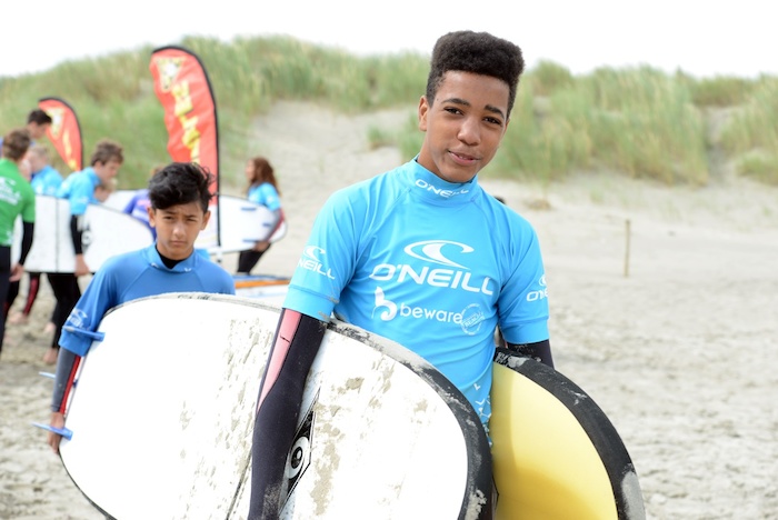 Een jongen wandelt met zijn surfplank naar de zee tijdens het watersportkamp
