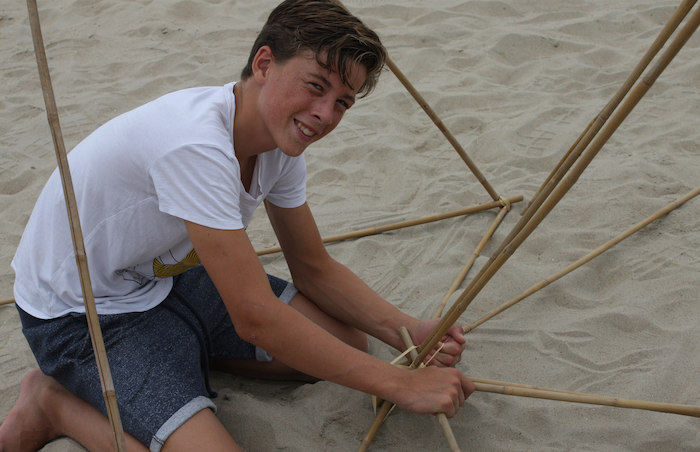Een jongen sjort stokken tijdens het surfkamp in Zeeland.