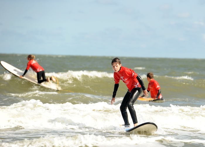 Jongen surft en kijkt naar camera op surfkamp herfstvakantie