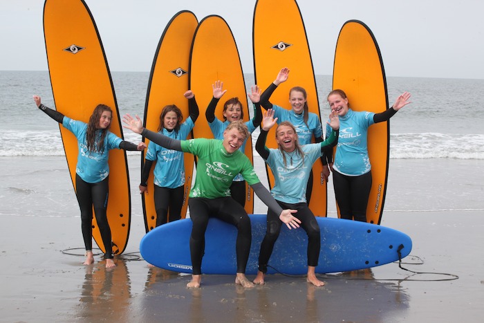Jongeren poseren voor hun surfboard voor de zee tijdens het surfkamp