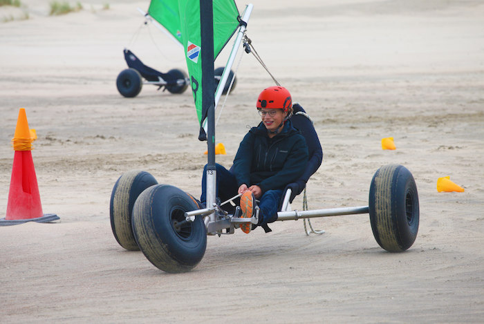 Een jongen is aan het blokarten op het strand tijdens het surfkamp in Zeeland.