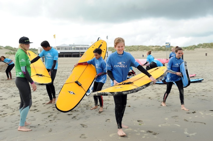 Een jongen wandelt met zijn surfboard terug naar de kampplaats tijdens het surfkamp
