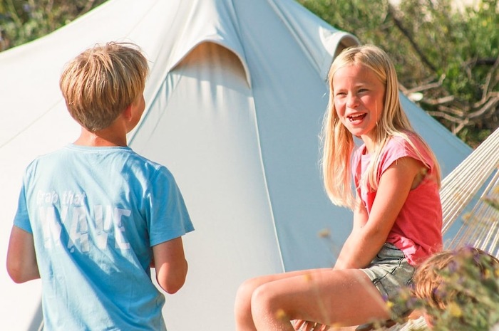 Kinderen relaxen voor hun tent op de kampplaats tijdens het watersportkamp