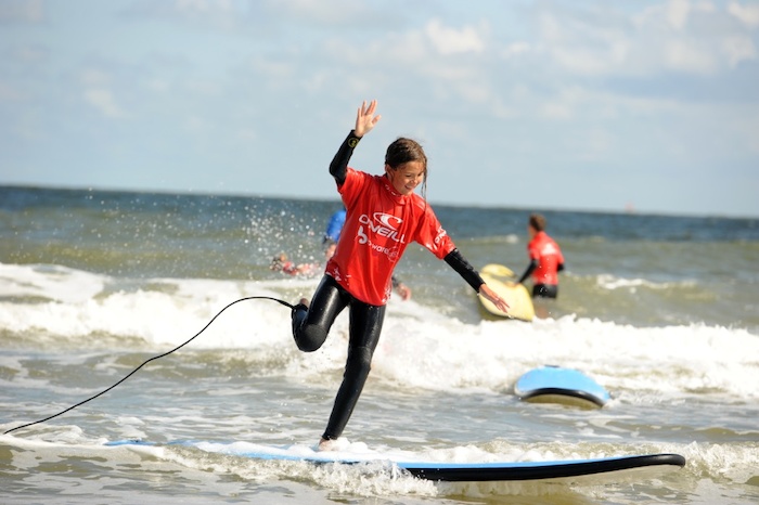 Een meisje staat op een been op haar surfboard tijdens het surfkamp