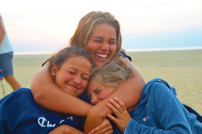 Drie meisjes knuffelen tijdens het surfkamp in Zeeland.