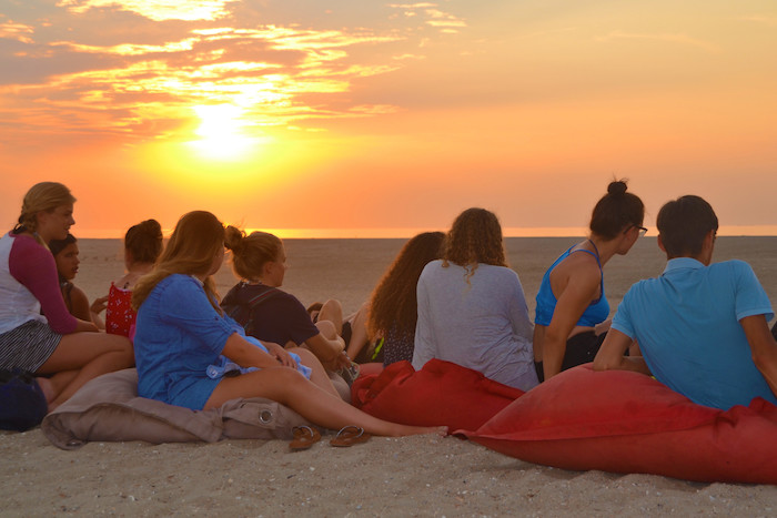 Groep meisjes kijkt naar de zonsondergang op surfkamp in Zeeland.