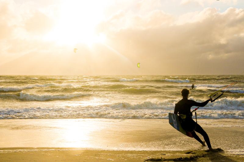 Kitesurfer op strand bij zonsondergang tijdens surfkamp zomervakantie