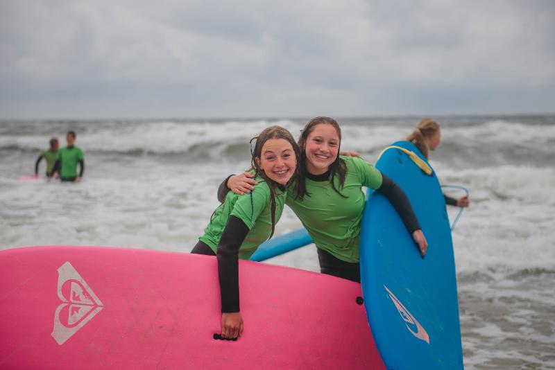 meiden in de zee met surfboards tijdens surfkamp Scheveningen