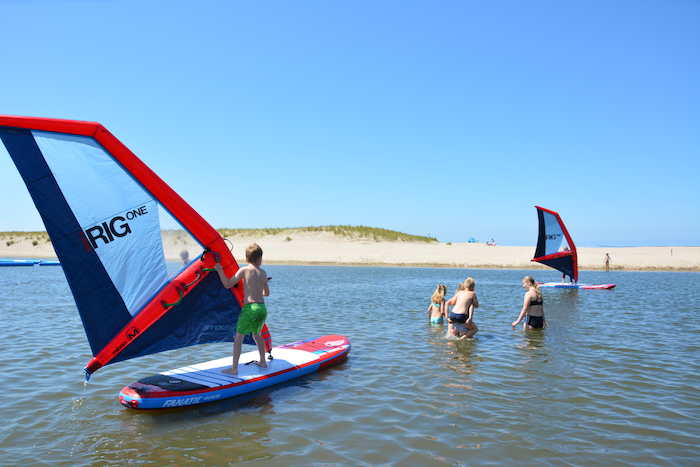 Kinderen begeven zich op watersportkamp al windsurfend richting de kust. 