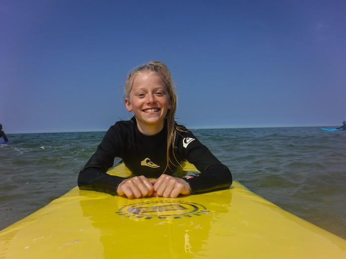 Meisje ligt tijdens zomerkamp Noord-Holland op surfboard en lacht. 