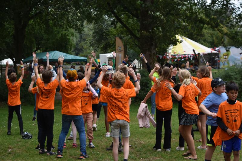 deelnemers doen een spel op het gras met een oranje shirt aan tijdens een jongerenvakantie nederland