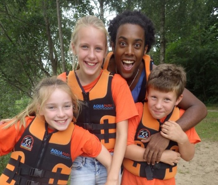 Kinderen en begeleider poseren lachend voor de camera op zomerkamp Nederland.