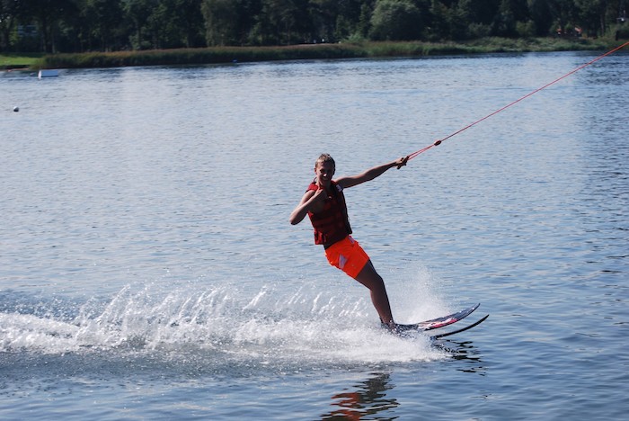 Een jongen glijdt over het meer op zijn wakeboard tijdens het wakeboardkamp in Gelderland