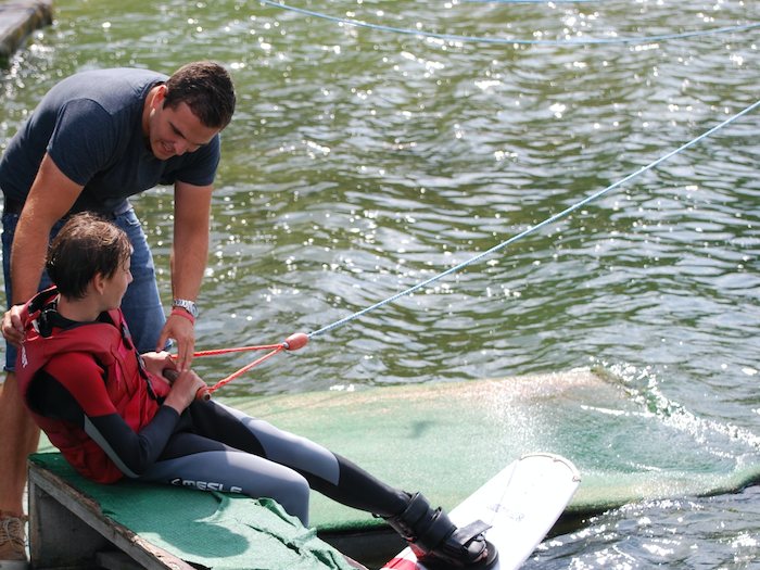 Een begeleider helpt een jongen op wakeboardkamp in Gelderland tijdens de zomer.