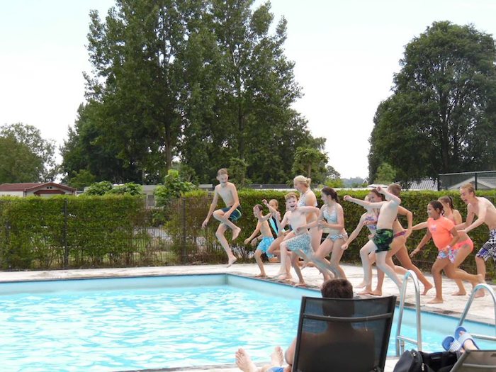 Deelnemers tienervakantie springen in zwembad.