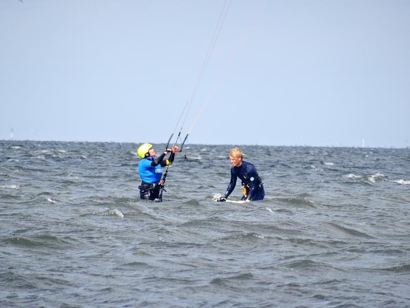 Twee deelnemers aan summer camp den haag zijn aan het kitesurfen in de golven
