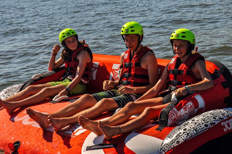 Met groene helmen en in rode reddingsvesten zitten deelnemers op boot tijdens watersportkamp Zuid-Holland