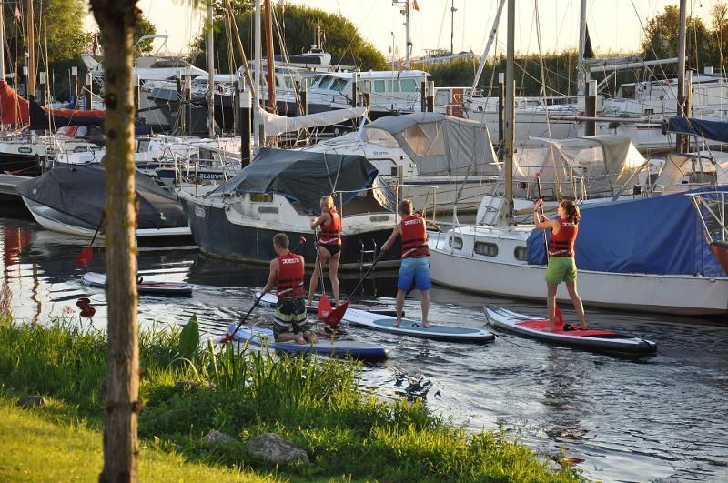 Deelnemers aan summer camps rotterdam suppen tussen boten tijdens zonsondergang