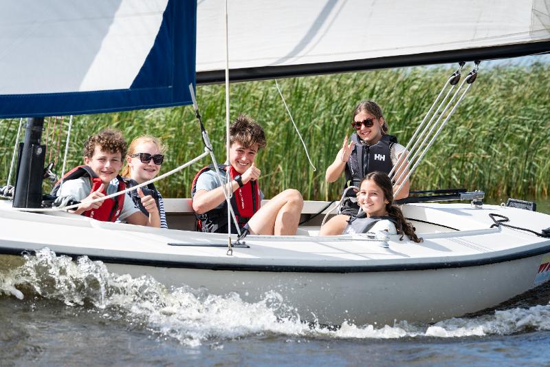 Een groep kinderen zit op een boot tijdens het surfkamp in Nederland voor 13 jaar