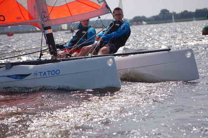 Een jongen en een meisje zeilen met een catamaran over het meer tijdens het zeilkamp friesland