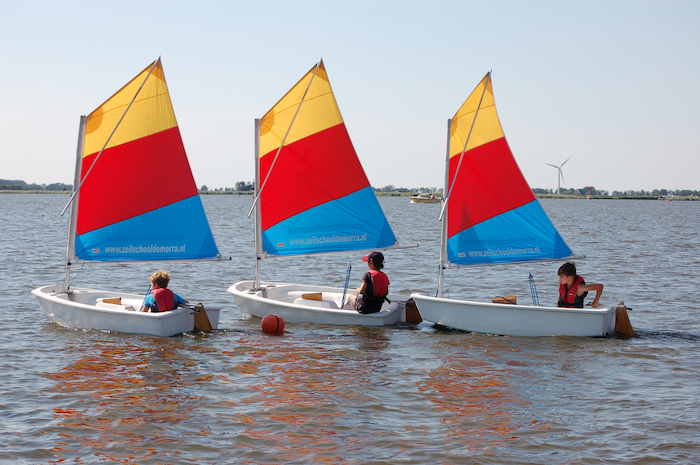 Drie kinderen zeilen met een optimist over het meer tijdens het zeilkamp in Friesland
