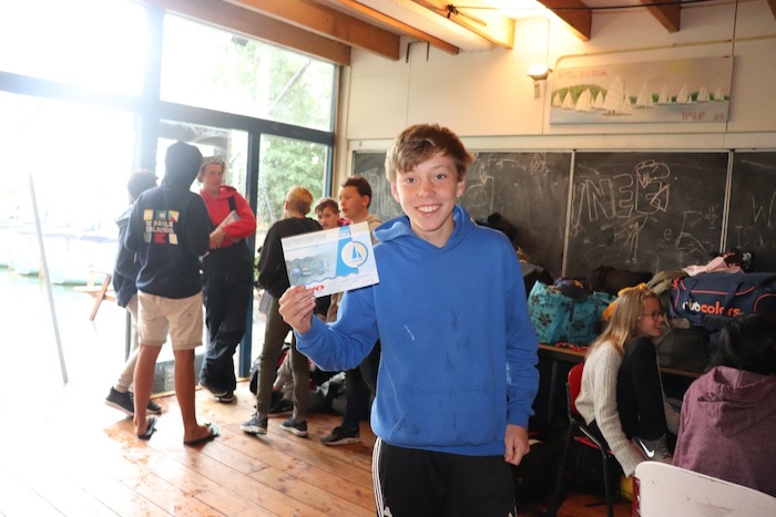 Een jongen toont het zeildiploma dat hij net behaalde tijdens het zeilkamp