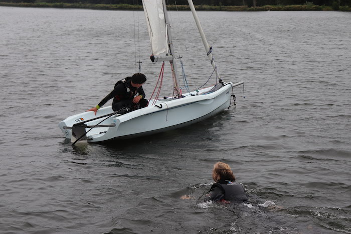 Een jongen zwemt naar een zeilboot tijdens het zeilkamp