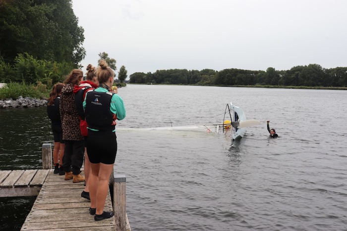 Meisjes staan aan de oever en kijken naar jongeren die windsurfen tijdens het zeilkamp