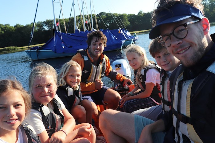 Deelnemers en kids zitten samen in zeilboot op zeilkamp zomer
