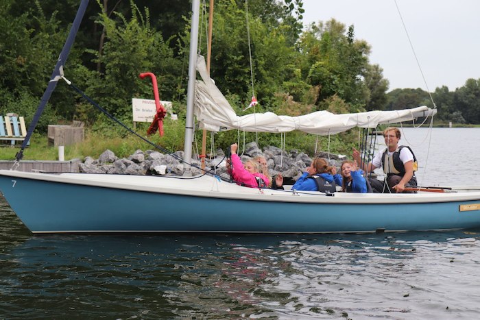 Kinderen zwaaien vanop hun boot naar de camera tijdens het zeilkamp