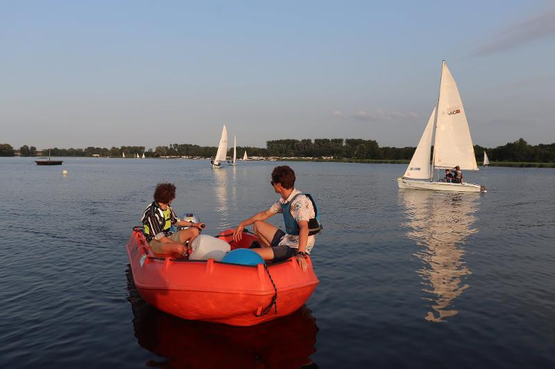 twee jongens varen op rode boot tijdens zonsondergang tijdens zeilkamp 