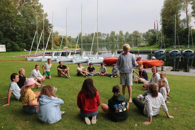 groepje deelnemers zit in een cirkel op het gras tijdens zeilkamp kinderen