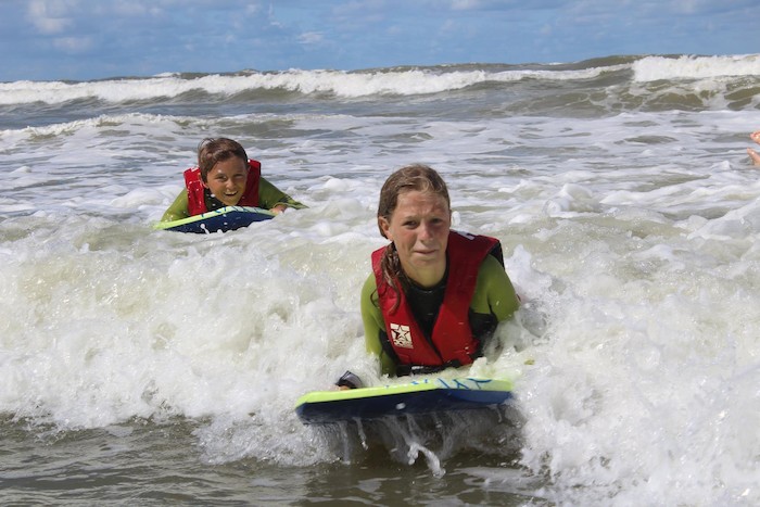 Jongen en meisje glijden tussen de golven op Zandvoorts surfkamp.