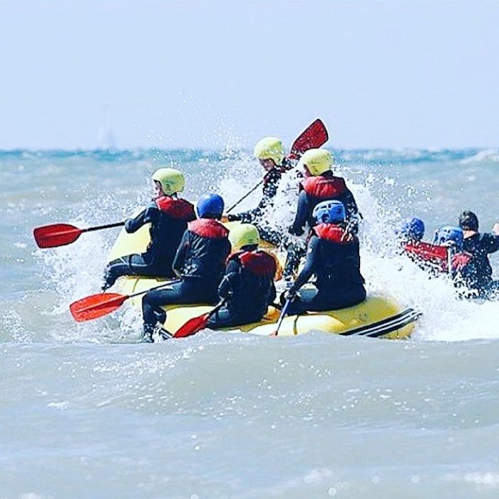 Jongeren zitten op raft met opspattend water op surfkamp in Bloemendaal. 