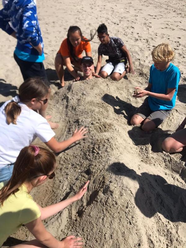meisjes graven begeleider in het zand op surfkamp zandvoort zomer