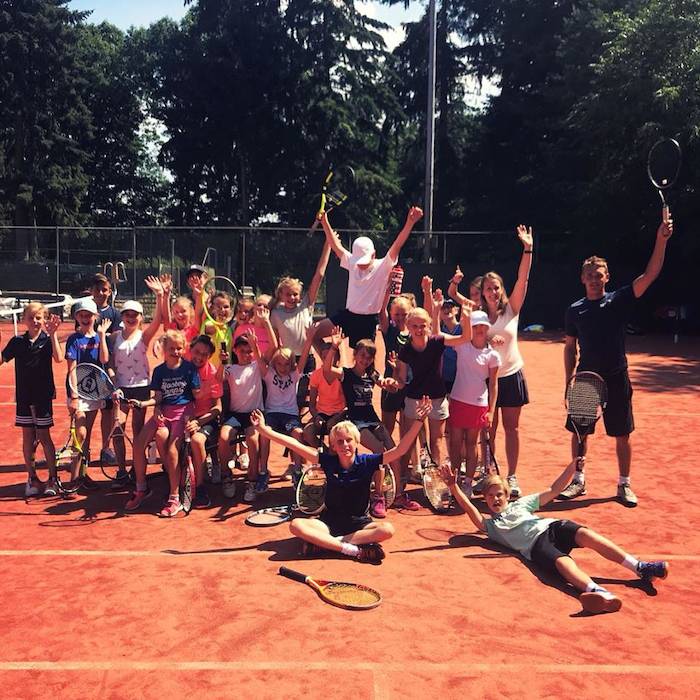 Kinderen poseren met hun tennisrackets op de tennisbaan