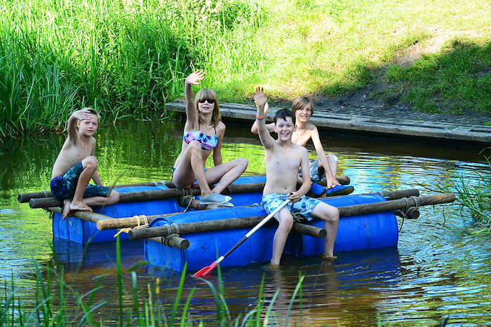 Kinderen zwaaien vanaf hun zelfgebouwde vlot waarmee ze de rivier oversteken tijdens het zomerkamp in Drenthe