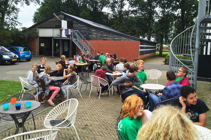 Jongeren genieten op het terras van hun lunch tijdens het zomerkamp in Drenthe