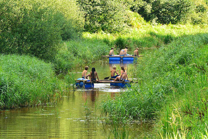 Jongeren varen de beek af met een zelfgebouwd vlot tijdens het computerkamp in Drenthe