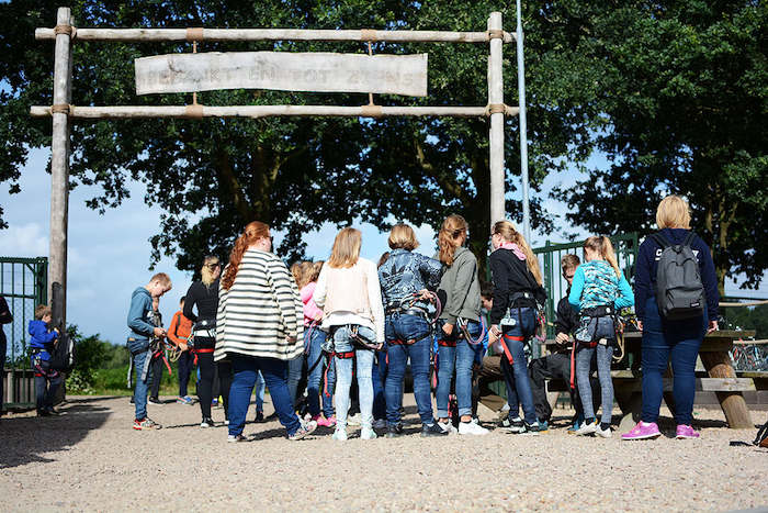 Meisjes in klimharnassen wachten bij klimparcours op zomerkamp in Drenthe.