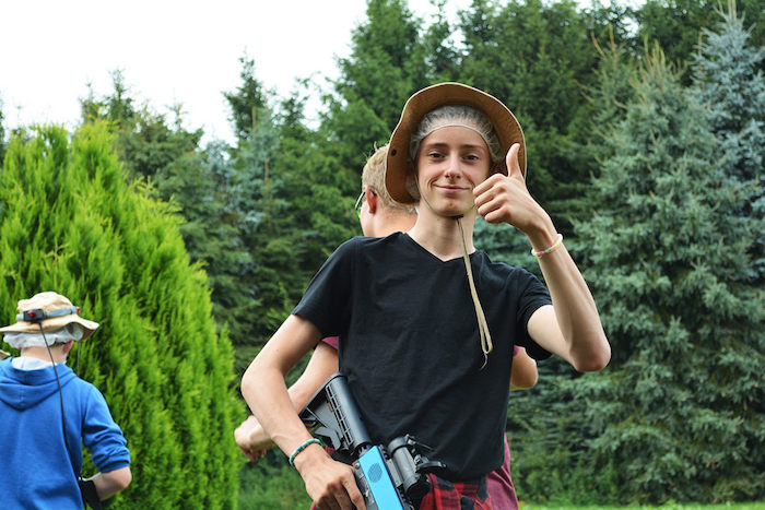 Jongen met geweer steekt duim op naar camera tijdens zomerkamp Drenthe.