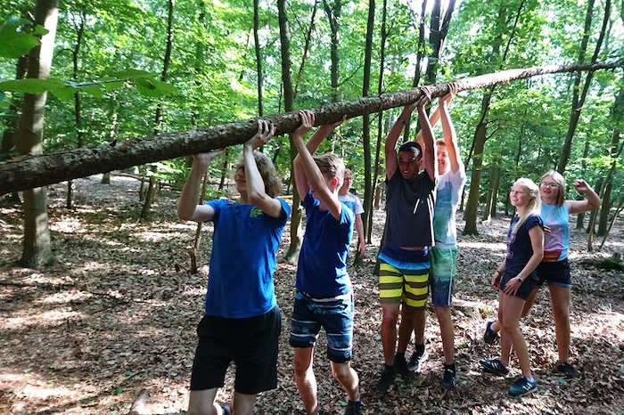 Jongens dragen een boomstam tijdens het survivalkamp.