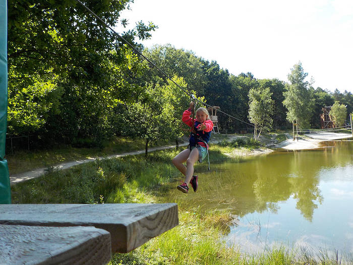 Een meisje hangt aan een zipline tijdens het zomerkamp in Drenthe.