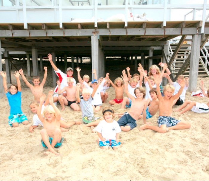 Groep kinderen poseert lachend in het zand.