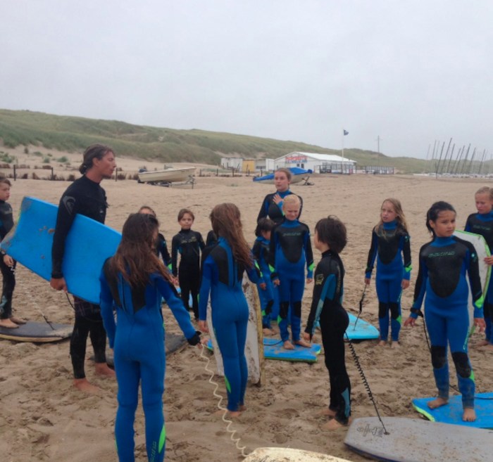 Kinderen in wetsuits poseren op strand in Nederland.