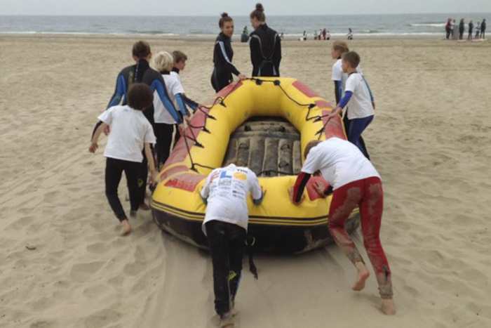 Jongeren duwen opblaasboot naar zee op jeugdkamp.