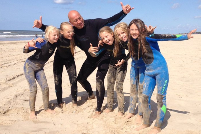 Meisjes en begeleider poseren in wetsuit op strand in Nederland.
